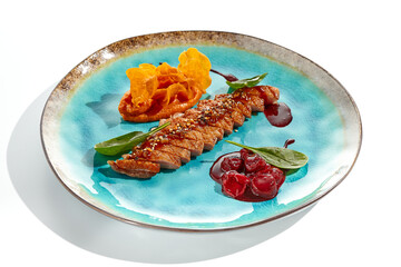 Roast duck breast with batata chips and cherry sauce isolated on white background. Delicious dinner - cooked duck meat with berry jam and sweet potato chips on trendy plate. Contemporary cuisine.