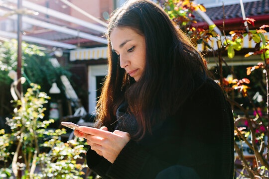 Young attractive woman checking smartphone in a garden in a winter day