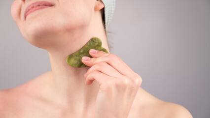 Close-up portrait of a young woman massaging her neck with a gouache scraper. 