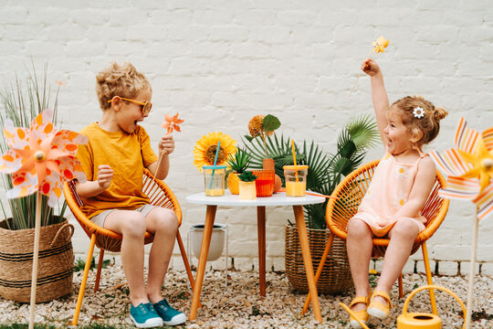 young siblings sitting on sunny colorful terrace playing with windmill