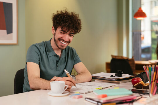 Positive man writing in notepad in coffee house