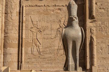 An ancient granite statue of a falcon in a crown on the background of the Temple of Horus in Edfu....