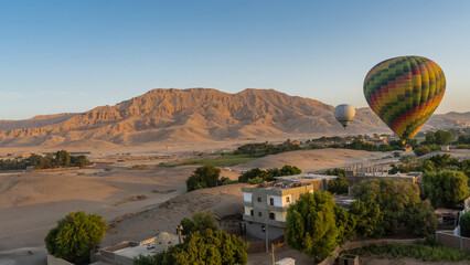 Bright balloons over Luxor. Residential buildings are visible among the trees. Sand dunes and a...