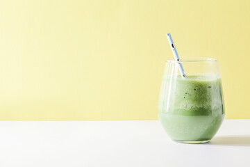 healthy green smoothie in glass with straw on yellow background. Vegetarian healthy lifestyle concept.refreshing drink copy space. quick snack
