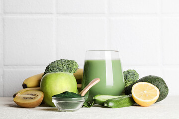 green smoothie in glass, spirulina powder, vegetables and fruits on white ceramic tile background. healthy, raw, vegan diet concept. copy space