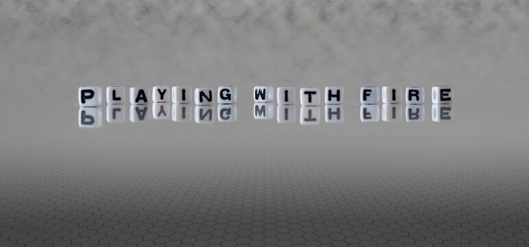 playing with fire word or concept represented by black and white letter cubes on a grey horizon background stretching to infinity