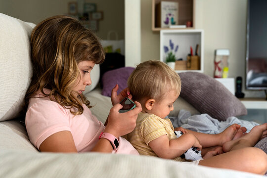 Girl using smartphone while baby sitting with brother