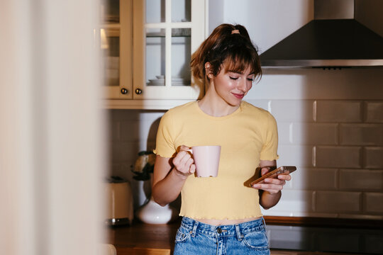 Woman browsing smartphone in kitchen at home