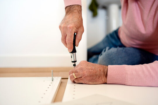Crop elderly man assembling furniture in flat