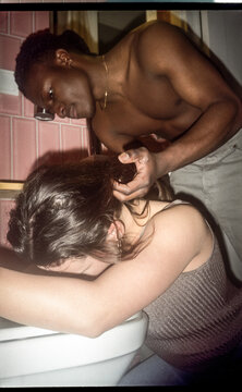 A guy helps his girlfriend who is puking over the toilet