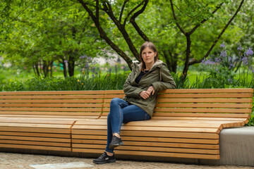Fototapeta premium Young woman sitting on a bench in a city park. Conceptual photo. Portrait of a young woman.