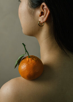 Orange resting on side profile of young woman