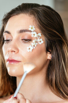 Woman makeup artist applying makeup on model face with flowers