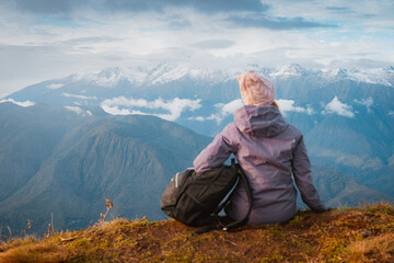 female tourist with a backpack enjoys the sunset at the top mountain