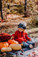 Little girl in a red coat sits in an autumn forest withe a basket of autumn fruits