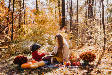 Mom and daughter sit on a mat with autumn fruits in the autumn forest