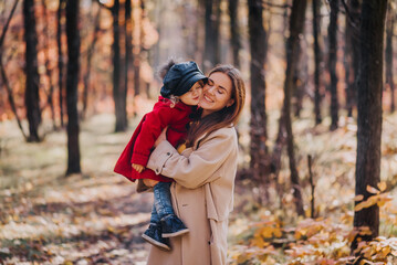 Mother kissing her daughter in a red coat in autumn forest