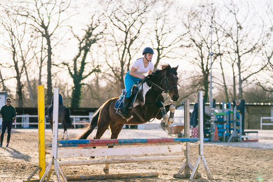 Active woman on horse jumping over barrier in ranch