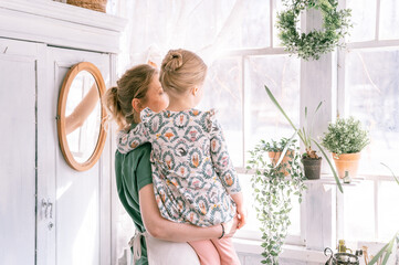 happy family mother with little kid daughter girl have fun in suburb countryside home life on sunny spring day. candid mom and children standing by the window with plant. people love and care moment