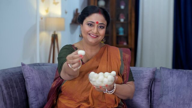 A Bengali female wearing a traditional Sari / Saree offering a Rasgulla - a tasty dessert  sugar  syrup. An attractive woman offering delicious Indian sweets with a smiling face - a festival time  ...