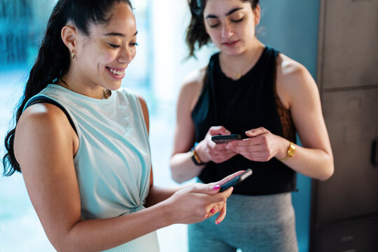 Positive sportswomen using smartphones in gym