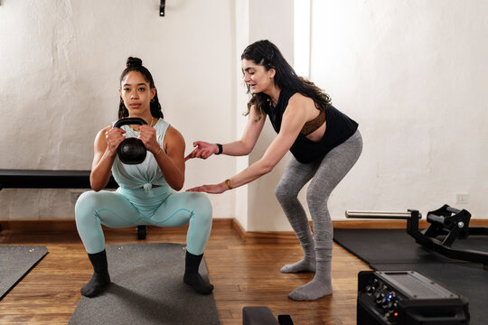 Trainer controlling sportswoman doing squat exercise
