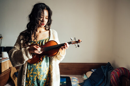 An asian young woman playing violin at home