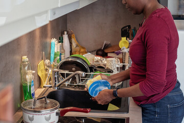 woman washing dishes in messy kitchen at home, hands close up