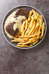Steak au poivre or pepper steak is a French dish that consists of a filet mignon, coated with coarsely cracked peppercorns served with french fries close-up in a plate on the table. Vertical top view 