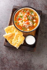 Spicy Uzbek mastava soup with lamb, rice and vegetables close-up in a bowl served with bread and sour milk on a wooden tray. vertical top view from above