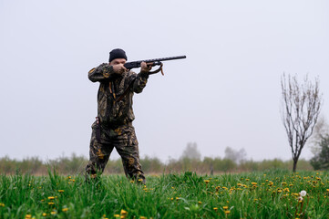 A male hunter with a rifle hunts and aims against the background of a foggy field