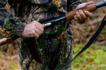 Hunter charges a cartridge into the chamber of a rifle close up on a background of reeds