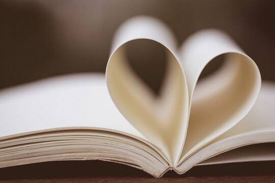 Close up heart shape from paper book on wooden table with vintage blur background