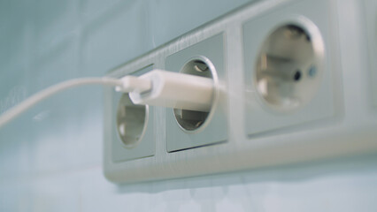 Man hand plug white phone charger adapter into wall socket