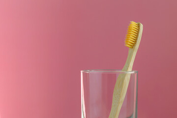 A glass with a toothbrush made of eco-friendly bamboo on a pink background. Space for text