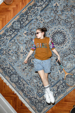 A teenage girl is lying on the carpet with a tennis racket