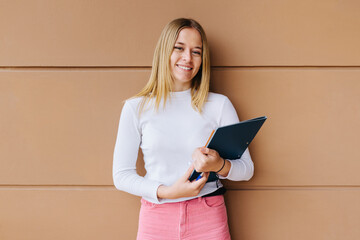Pretty young girl holding folder over brown wall