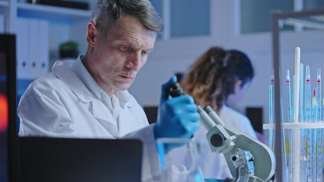 Medical laboratory scientist examining infected cell under microscope, research