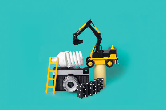 Composition with camera, lightbulb, domino, ladder and toy excavator
