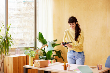 Glad woman taking photo of cosmetic bottles