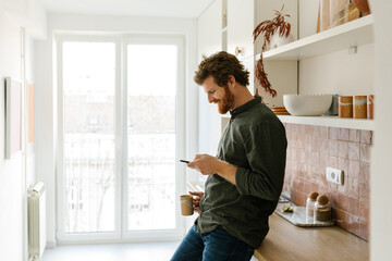 Happy mature male using phone and holding cup of coffee