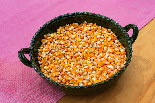 Yellow corn kernels in a green clay pot on a wooden table 