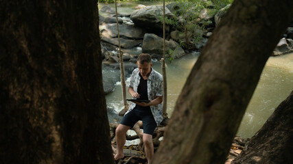 A middle-aged man in the middle of the forest, trees, nature and using a laptop.