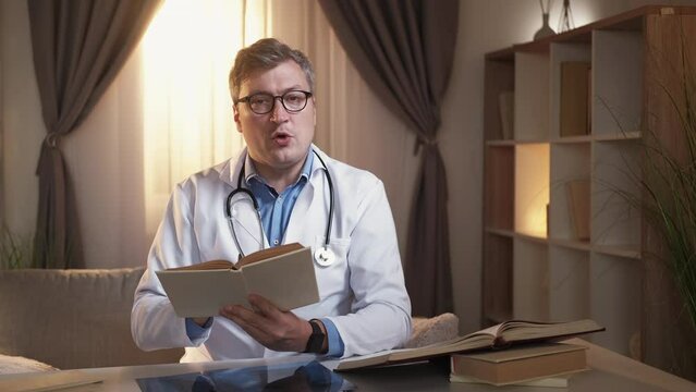 Book research. Male doctor. Online consultation. Inspired smart man studying encyclopedia information for making correct diagnosis sitting light room interior.