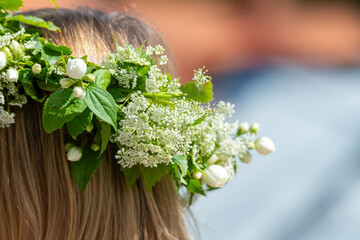 Woman with a flower wreath on her head. Midsummer celebration, a Swedish feast and tradition in June. Photography taken from behind, blurred bokeh background, copy space, place for text.	