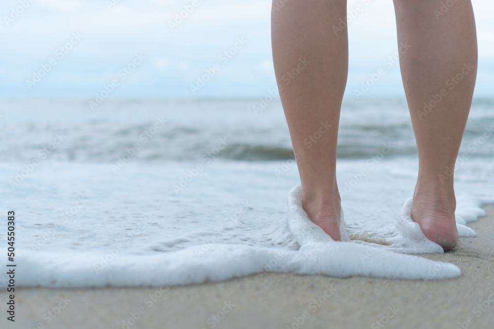 Wall mural On a sand tropical beach with a blue sky background, a woman's feet walk slowly and relax.