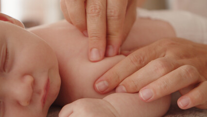 Mother doing massage on her healthy sleeping infant baby. Small caucasian newborn resting and...