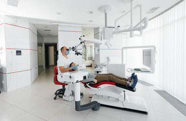 A young dentist examines and treats the teeth of a young guy in modern white dentistry using a microscope. Dental prosthetics, treatment and teeth whitening. Prevention of caries.