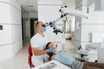 A young dentist examines and treats the teeth of a young guy in modern white dentistry using a microscope. Dental prosthetics, treatment and teeth whitening. Prevention of caries.
