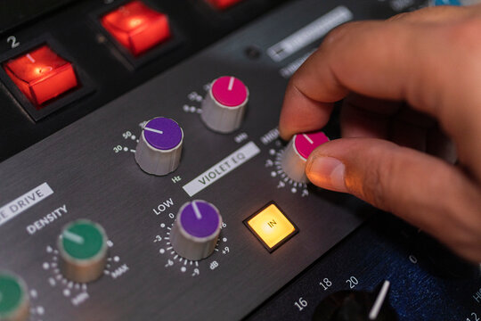 closeup of male right hand moving a volume dial on an audio console 